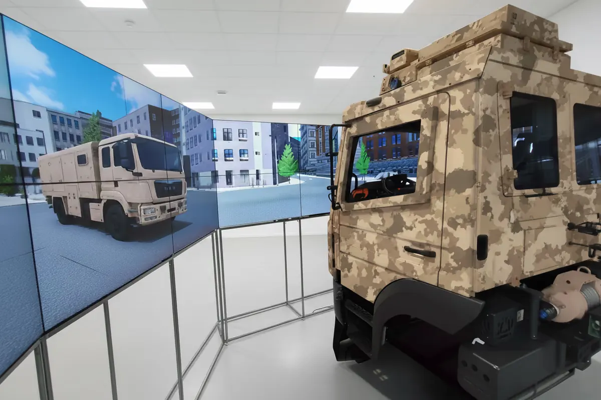 Ámbito militar Simulador de conducción militar SIFAT: cabina de conducción con pintura de camuflaje frente a una gran pantalla con una escena urbana: formación en conducción para las Fuerzas Armadas